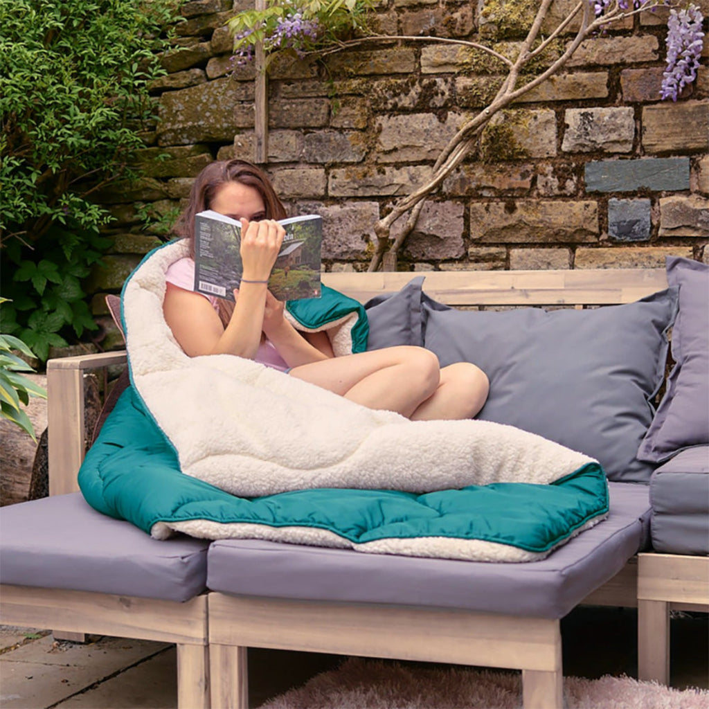 A woman in garden reading sat on a Night Lark/ Night Owl  Outdoor Sherpa Fleece Duvet In Cabin Green